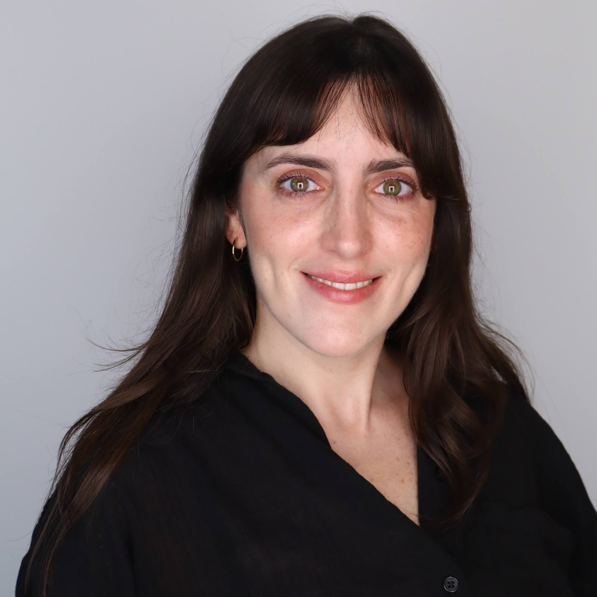 Woman with dark hair, green eyes, and freckles smiles, wearing a black shirt.